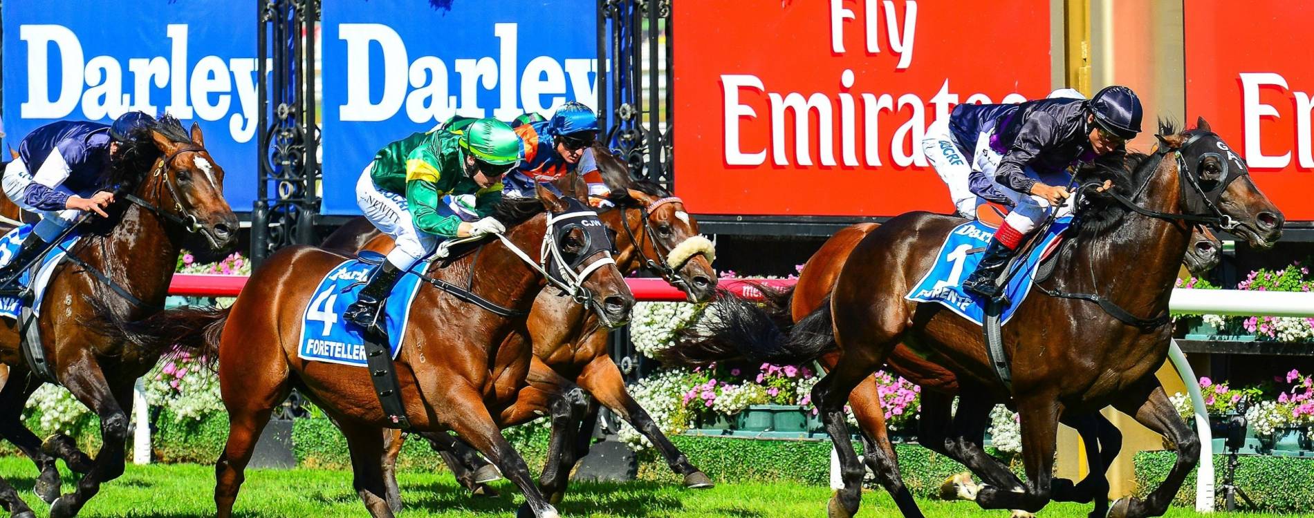 Horses racing past Emirates-branded signage at Flemington Racecourse during Emirates Day Racing